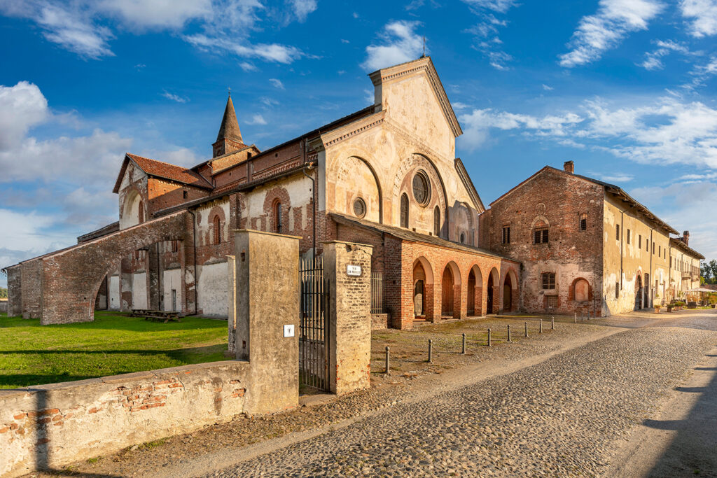 vista esterna dell'abbazia di Staffarda, con facciata della chiesa e viale in ciottolato.