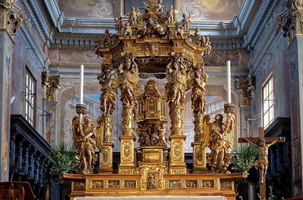 Primo piano dell'altare maggiore con affreschi e decorazioni ai lati del presbiterio.