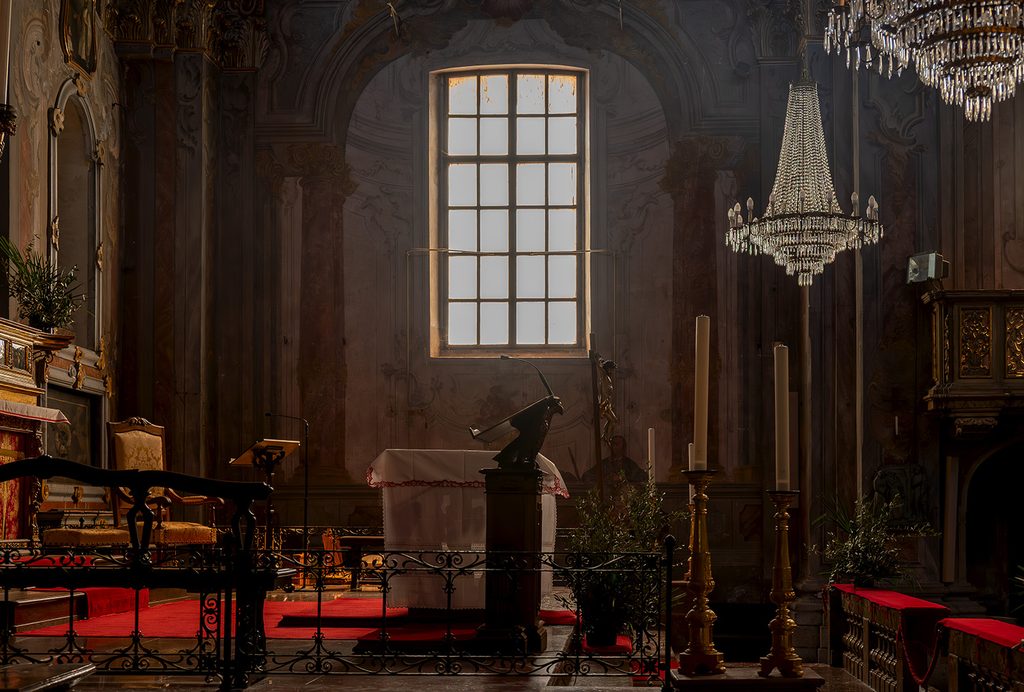 Interni della chiesa di San Bartolomeo a Borgomanero, vicino al presbiterio, con lampadari antichi e giochi di luve e ombre con la finestra.