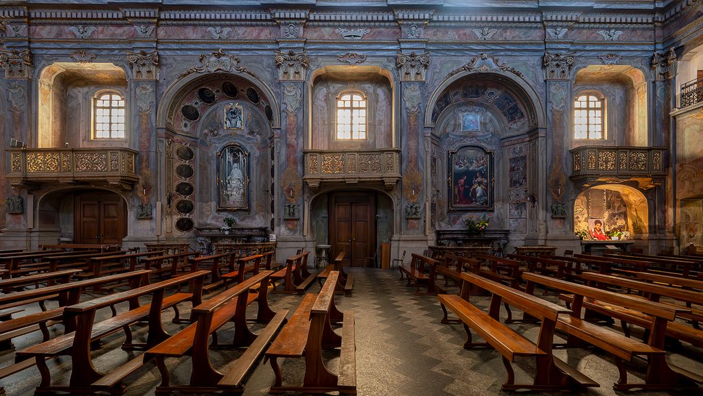 Navata destra della chiesa di san Bartolomeo, con dipinti e affreschi e la luce del sole che penetra dalle finestre.